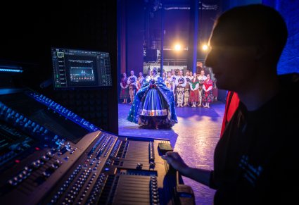 Na pierwszym planie Dźwiękowiec przy konsoli, w tle Artyści występujący w spektaklu