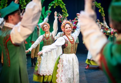 Zbliżenie na uśmiechnięte Artystki w kostiumach lubuskich w trakcie wykonywania choreografii tanecznej z elementami dekoracyjnymi na scenie
