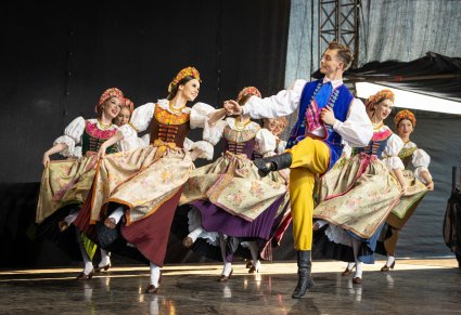 Na scene grupa Artystów Tancerzy w kostiumach rozbarskich w trakcie wykonywania choreografii tanecznej