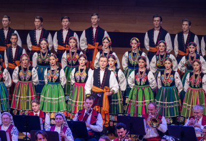 Na pierwszym planie Solista, w tle Artyści Chóru w kostiumach łowickich. Przed Chórem widoczna część Orkiestry w kostiumach wilanowskich