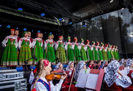 Na pierwszym planie część członków orkiestry, na scenie Artyści w rzędzie w kostiumach kurpiowskich