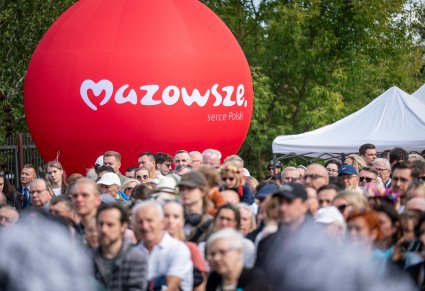 Na pierwszym planie duży, czerwony balon z logo Mazowsze serce Polski, na zdjęciu również widoczna część widowni