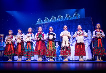 Przedszkolaki w kostiumach ludowych trzymające w rękach pluszowe maskotki, za nimi część postaci ze spektaklu