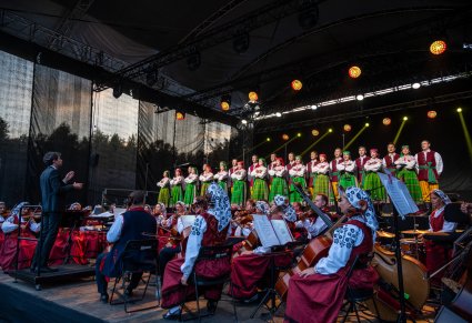 Artyści z chóru w kostiumach kurpiowskich i orkiestra z Dyrygentem na scenie