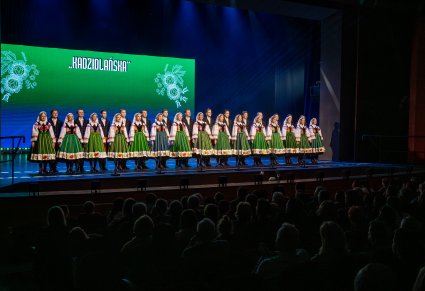 Na scenie Artyści Chóru w kostiumach kocierzewskich w trakcie śpiewu, widoczna część publiczności