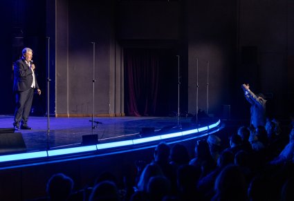 Na scenie uśmiechnięty Dyrektor zespołu, widoczna również część publiczności