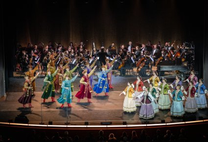 Na scenie grupa Artystów w kontuszach w trakcie wykonywania choreografii tanecznej, w tle Orkiestra