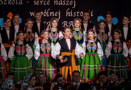 Artysta chóru w kostiumie łowickim podczas wykonywania utworu, w tle widoczny chór