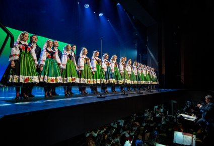 Widok na Artystów Chóru w kostiumach kocierzewskich w trakcie śpiewu. Widoczna Orkiestra w orkiestronie