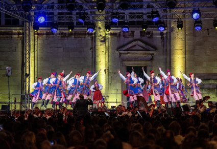 Widok na publiczność i scenę na której Artyści w kostiumach krakowskich wykonują choreografię taneczną