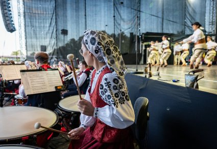 Zbliżenie na muzyka orkiesty grającego na kotłach, w tle balet podczas tańców góralskich