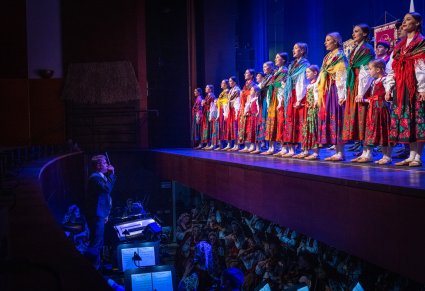 Widoczny orkiestron z Muzykami a na scenie Artyści z przedszkolakami w kostiumach ludowych