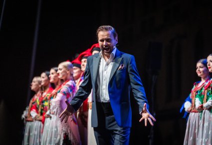 Na pierwszym planie Solista a w tle Artyści w kostiumach ludowych