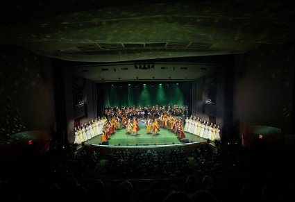 Szeroki widok na wyciemnioną publiczność i oświetloną scenę. Na scenie Artyści Baletu, Chóru i Orkiestra.