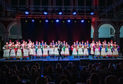 Na pierwszym planie solista a w tle Artyści w kostiumach ludowych