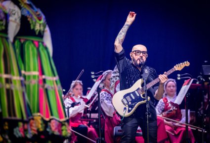 Zbliżenie Na Solistę zespołu Kombii w tle widoczna część Orkiestry w kostiumach łowickich