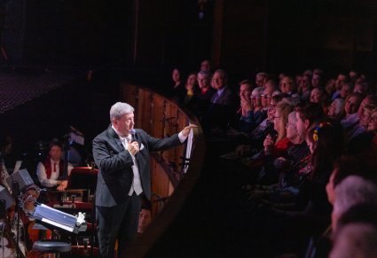 Dyrektor zespołu, dyrygujący koncert z orkiestronu, zwrócony w stronę publiczności w trakcie przemówienia