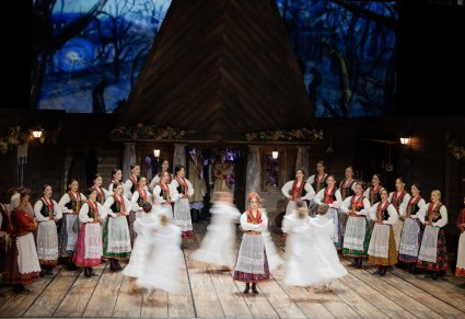 Na ąrodku sceny solistka w kostiumie krakowskim wkoło niej Artystki w zwiewnych, białych kostiumach, po bokach sceny Artystki Chóru w kostiumach krakowskich