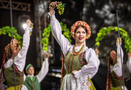 Zbliżenie na Artystkę Baletu w kostiumie lubuskim podczas wykonywania choreografii tanecznej, wykorzystując rekwizyt w tym przypadku kiść winogrona