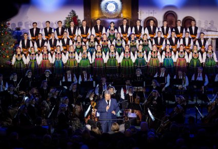 Na pierwszym planie Dyrektor zespołu "Mazowsze" w tle Orkiestra w kostiumach wilanowskich, a za nią w 3 rzędach Artyści Chóru w kostiumach łowickich