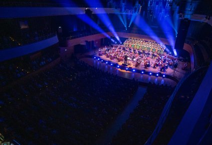 Widok na oświetloną scenę, na scenie Artyści Chóru w kostiumach łowickich wraz z Orkiestrą w kostiumach wilanowskich