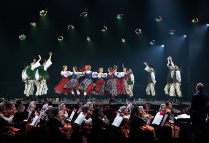 Na scenie Artyści w kostiumach spiskich w trakcie wykonywania choreografii tanecznej, niżej Artyści Orkiestry w kostiumach wilanowskich