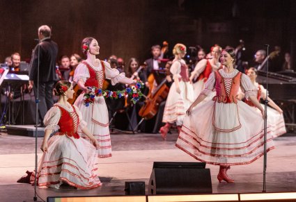 Na scenie grupa Artystek Tancerek w inspirowanych sukniach czerwono białych, wykonujące choreografię taneczną