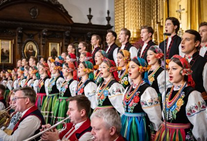 Zbliżenie na Artystów Chóru w kostiumach łowickich, niżej widoczna część Orkiestry w kostiumach wilanowskich grająca na instrumentach dętych