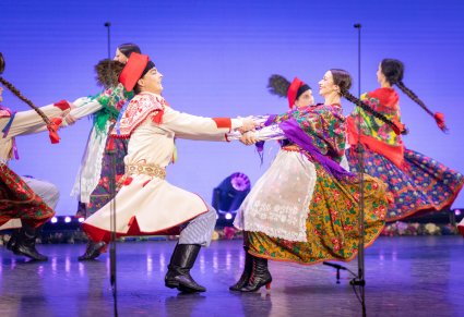 Na pierwszym planie para Artystów w kostiumach krakowskich w trakcie wykonywania choreografii tanecznej