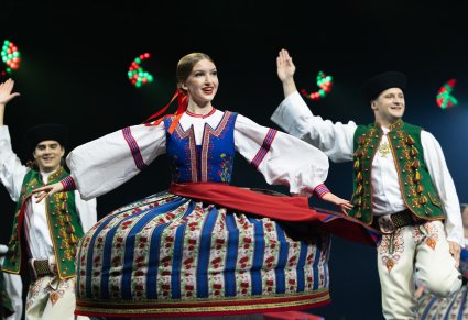 Zbliżenie na Artystkę w kostiumie spiskim w trakcie wykonywania obrotów, za Artystką dwóch Artystów również w kostiumach spiskich