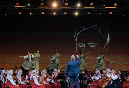 Na pierwszym planie Dyrygent zwrócony w stronę orkiestry w kostiumach wilanowskich i Artystów Baletu w kontuszach, którzy wykonywali na scenie choreografię taneczną