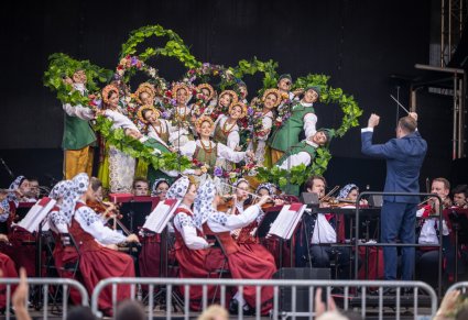 Na scenie Artyści w kostiumach lubuskich wykonujący finałową figurę taneczną, przed nimi Dyrygent, zwrócony w ich stronę, niżej sceny Artyści Orkiestry w kostiumach wilanowskich grający na instrumentach