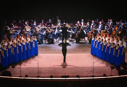 Na środku sceny Solista, po bokach sceny Artyści Chóru w kostiumach współczesnych, a na tyłach sceny Orkiestra