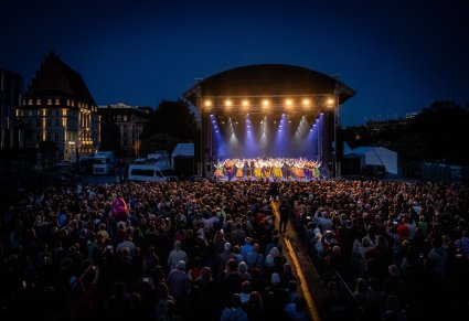 Szeroki widok na scenę i publiczność. Na scenie Artyści zespołu "Mazowsze" w trakcie wykonywania choreografii tanecznej