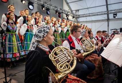 Muzycy instrumentów dętych w kostiumach wilanowskich oraz w tle chór w kostiumach łowickich