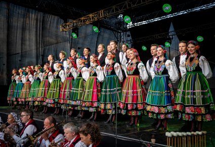 Na scenie Artyści z chóru w kostiumach łowickich a na dole część orkiestry