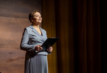 Zbliżenie na Konferansjerkę, ubraną w szary, elegancki kostium