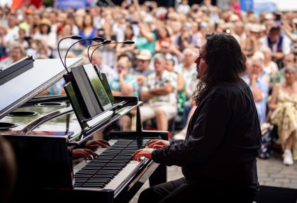 Widok na akustyka grającego na instrumencie a w tle publiczność