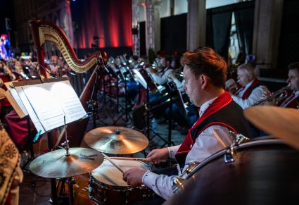 Zbliżenie na Artystę z Orkiestry i jego instrument i nuty, w tle reszta część orkiestry