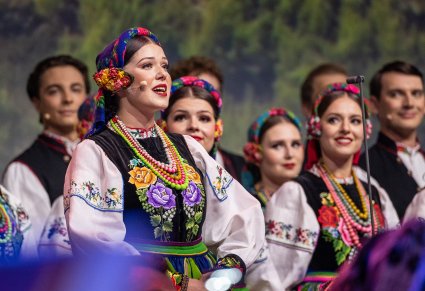 Na pierwszym planie duże zbliżenie na solistkę a za nią część Artystów z chóru w kostiumach łowickich
