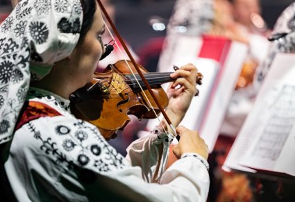 Zbliżenie na Artystkę Orkiestry w kostiumie wilanowskim grającą na instrumencie smyczkowym