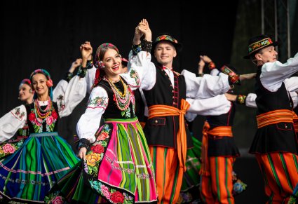 Artyści w kostiumach łowickich na scenie wykonujący choreografię taneczną