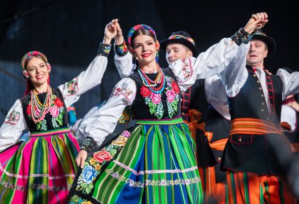 Dwie pary Artystów w kostiumach łowickich na scenie w trakcie wykonywania choreografii tanecznej