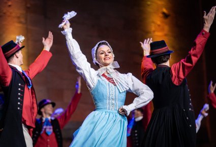 Zbliżenie na Artystkę na pierwszym planie a na drugim Artyści w kostiumach szamotulskich w trakcie wykonywania choreografii tanecznej