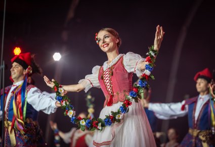 Na pierwszym planie para Artystów w kostiumach Rondo. Artystka w rękach trzyma dekorację z kwiatów