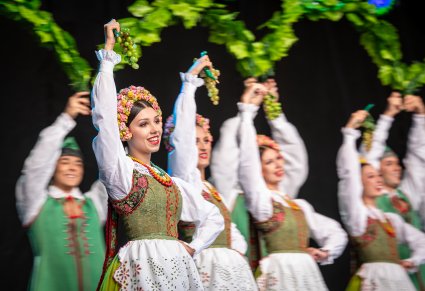 Uśmiechnięci Artyści w kostiumach lubuskich na scenie trzymający dekoracje w górze składającą się z pędów winogron