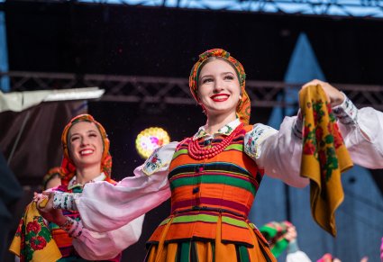 Przybliżenie na dwie Artystki na scenie w kostiumach łowickich trzymające w dłoni chustę