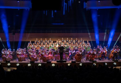 Na pierwszym planie Dyrygent zwrócony w stronę Orkiestry i Artystów Chóru.