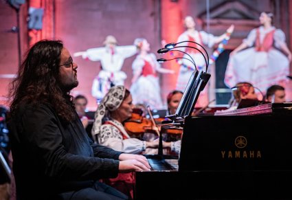 Na pierwszym planie zbliżenie na akompaniatora a w tle część Orkiestry i chóru