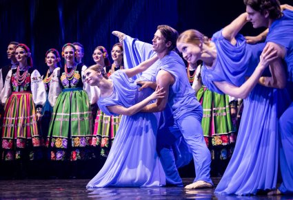 Na pierwszym planie Artyści Baletu w kostiumach współczesnych podczas wykonywania choreografii tanecznej, w tle widoczna część Artystów Chóru w kostiumach łowickich